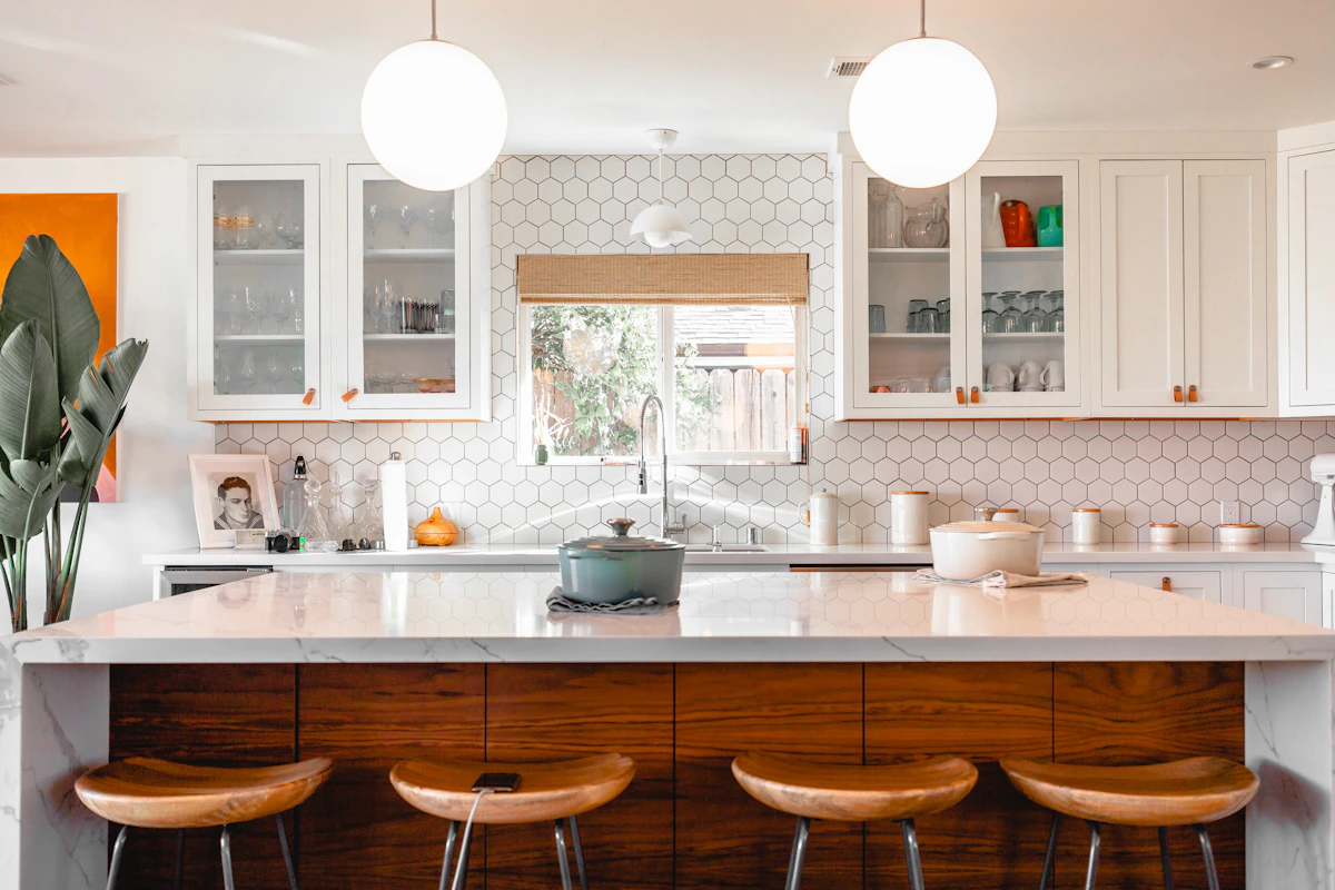 White kitchen with an island, wooden stools and pendant lights